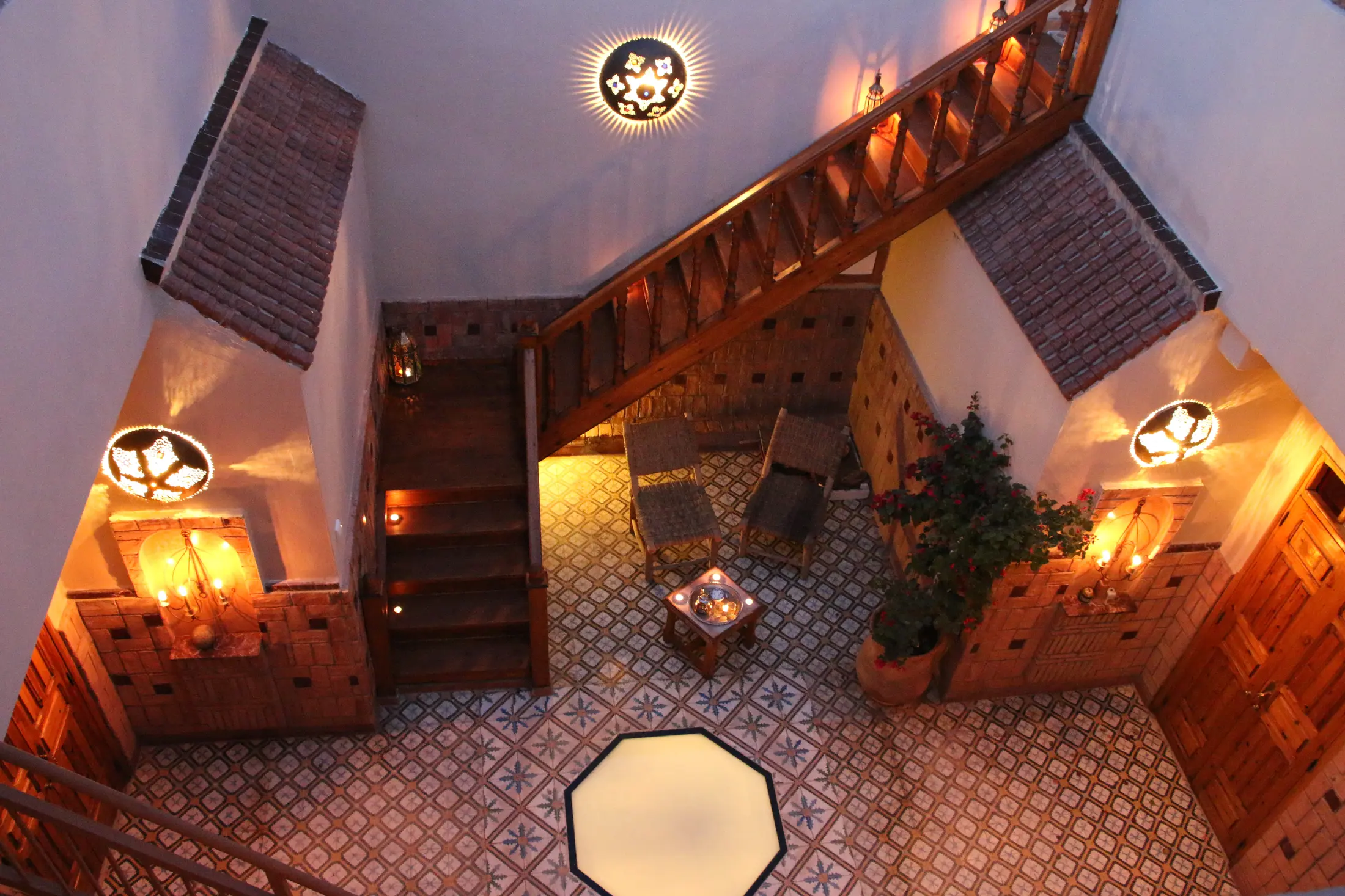 The zellige courtyard seen from the roof at dusk, with its lit cedar staircase and lanterns