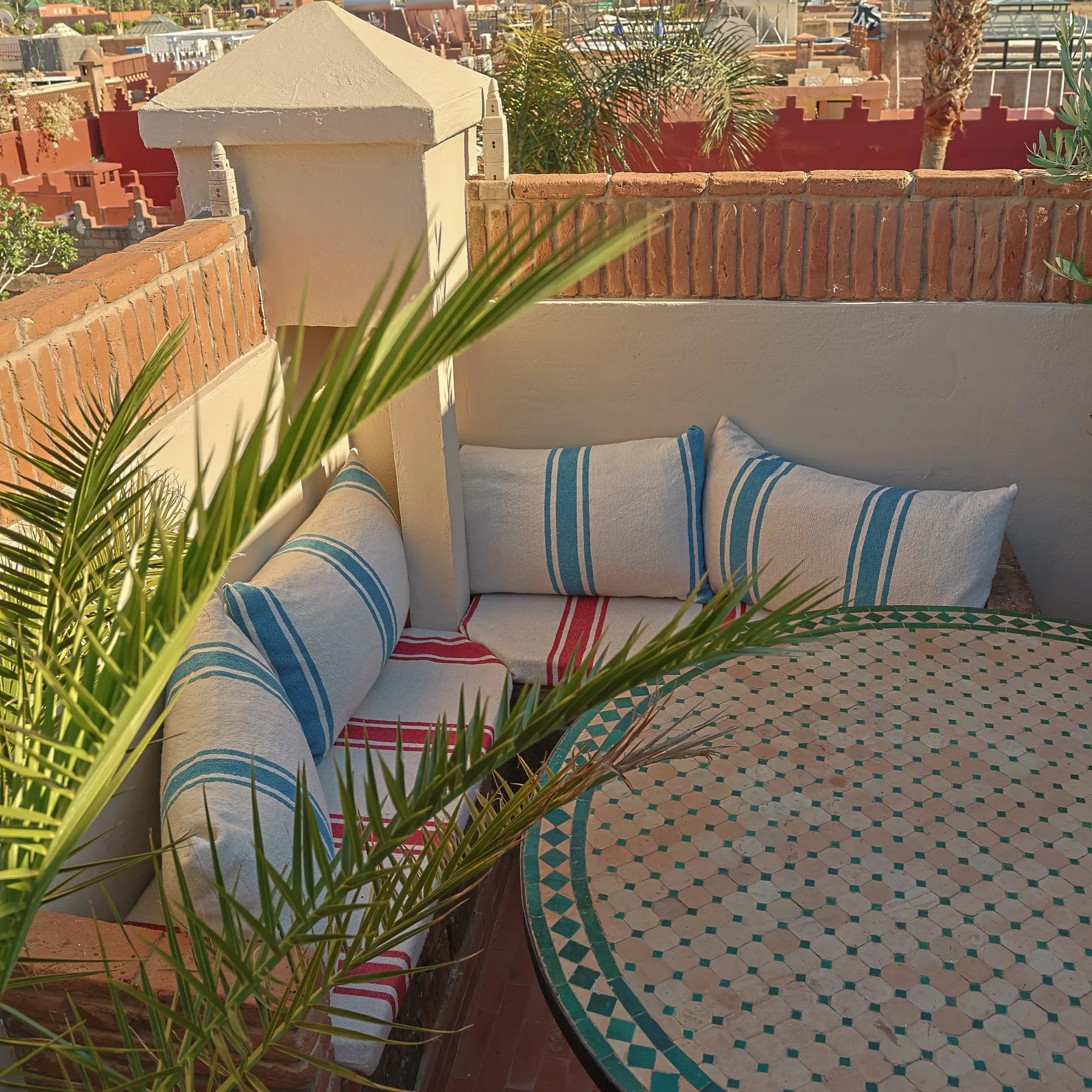 A cushioned corner banquette and mosaic table on the terrace, shaded by a palm