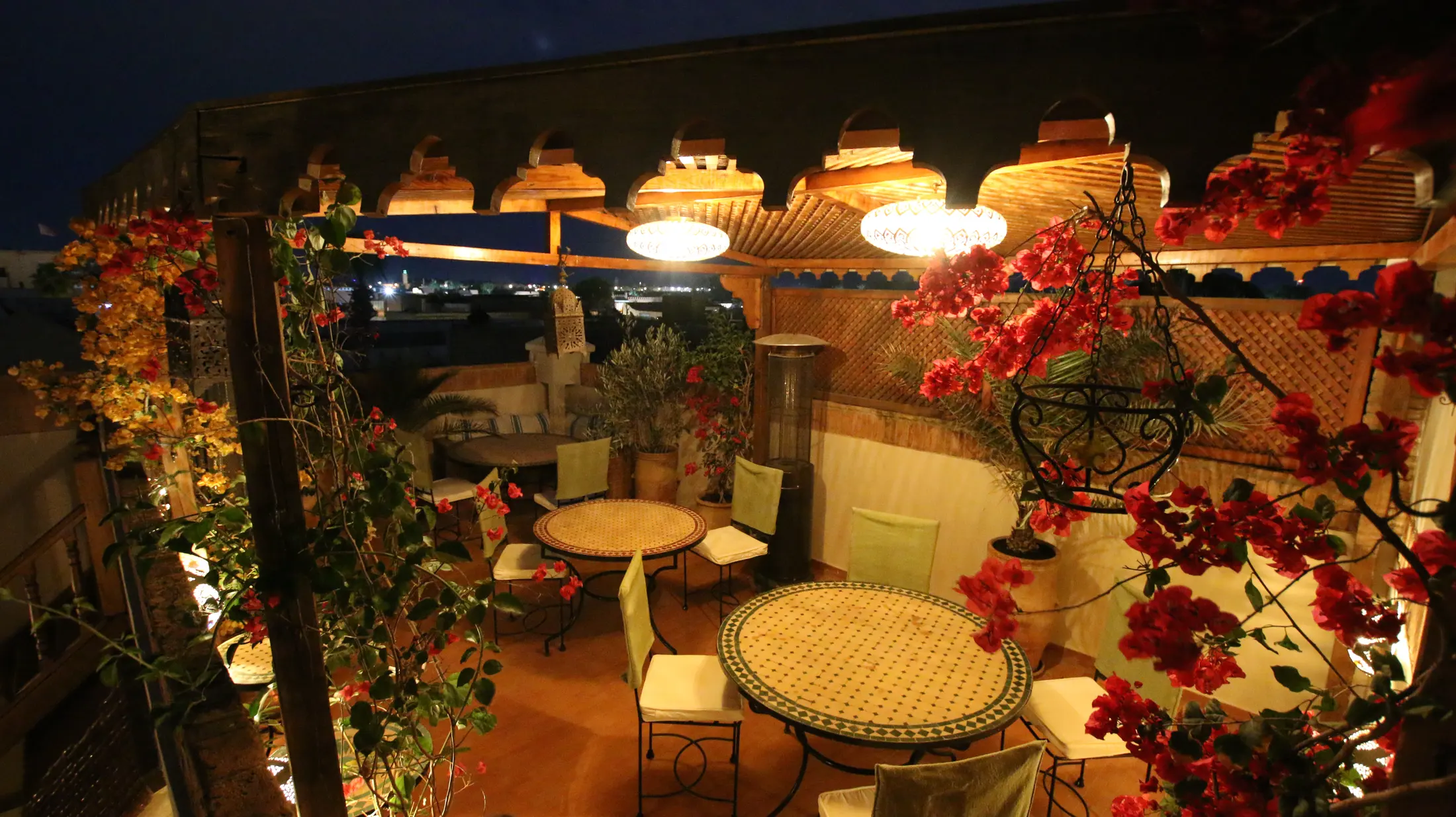 The Majlis Dining Terrace at night, tables set beneath lanterns and bougainvillea