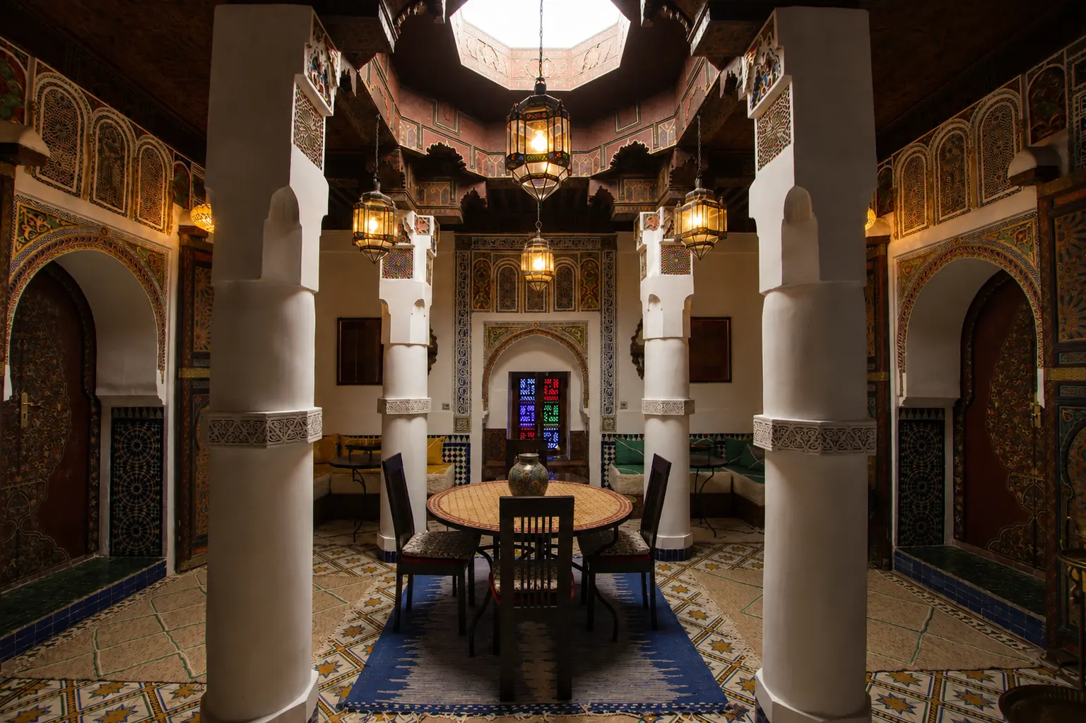 The Grand Salon on its central axis: white columns, carved arches, hanging lanterns and a round table beneath the painted ceiling
